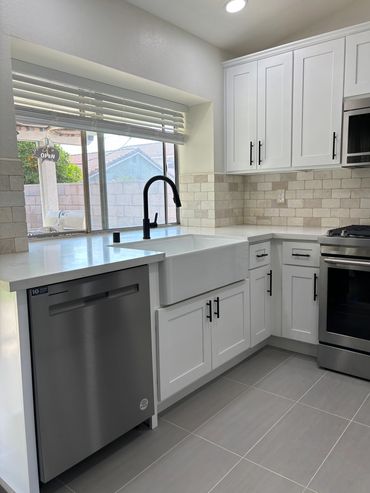 Modern white kitchen with stainless steel appliances and farmhouse sink.