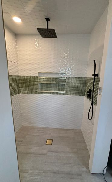 Modern walk-in shower with white and green tiles and black fixtures.