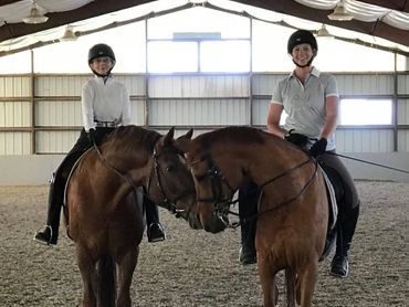 Two riders on horses facing each other inside an indoor riding arena.