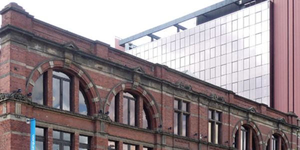 Historic red brick building with arched windows and modern glass skyscraper behind it.
