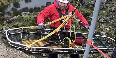 Rescue workers perform a cliffside rope rescue near a body of water.