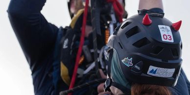 Two climbers working with ropes and wearing helmets, one with red devil horns.