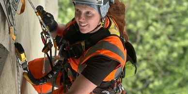Rescue worker in orange gear rappelling down a concrete wall with safety equipment.