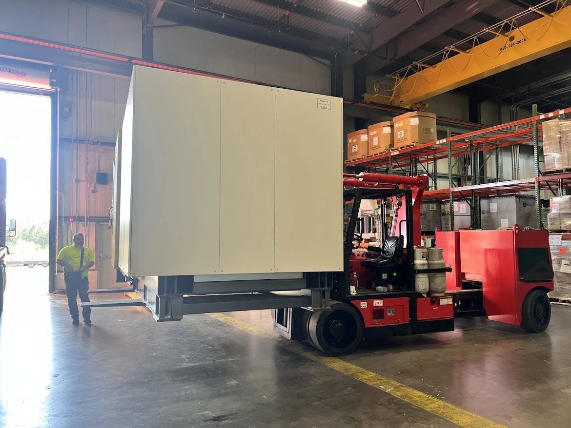 Red forklift lifting large white container inside warehouse.