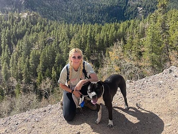 A black dog stands next to a crouched woman