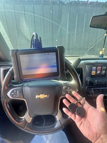 Diagnostic device on Chevrolet steering wheel with two car keys in hand.