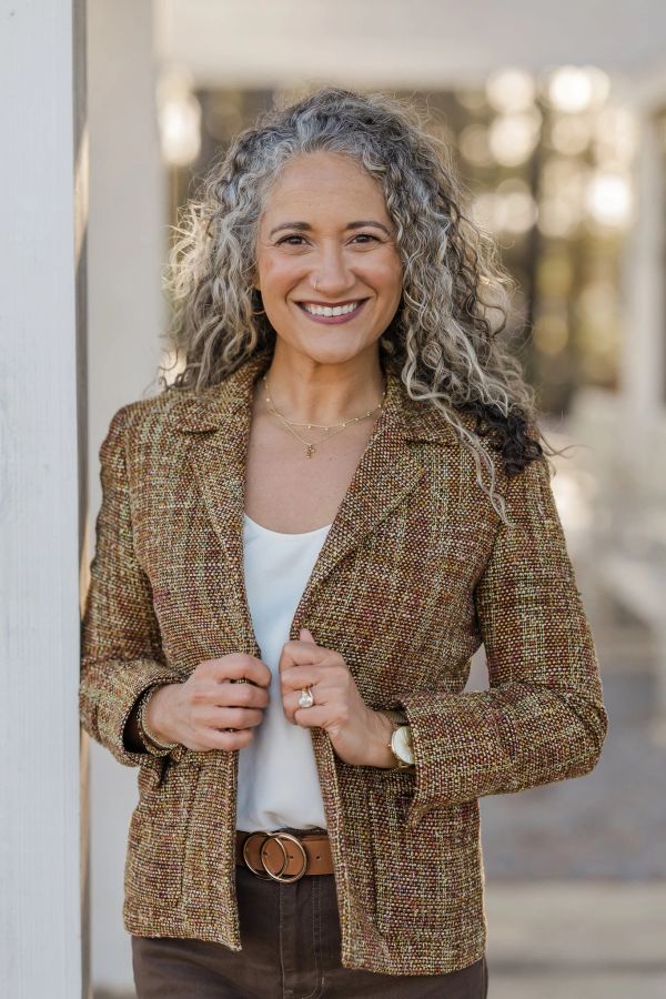 Smiling woman with curly gray hair in a tweed jacket.