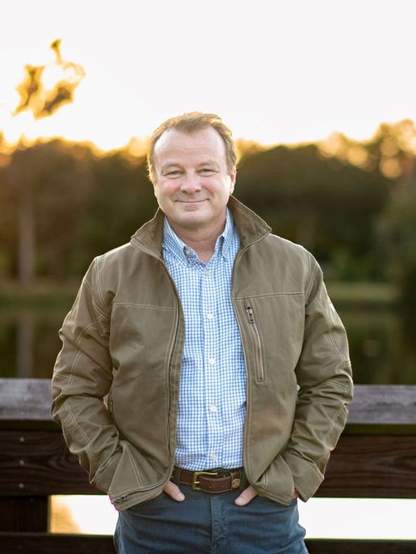 Man standing outdoors near a wooden railing, smiling.