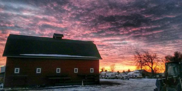 Sunset behind a barn with snow-covered ground.
