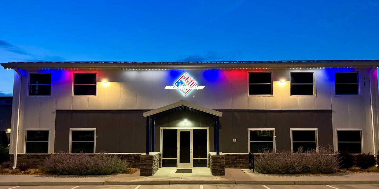 Front entrance of a building with colorful lights and a logo at dusk.