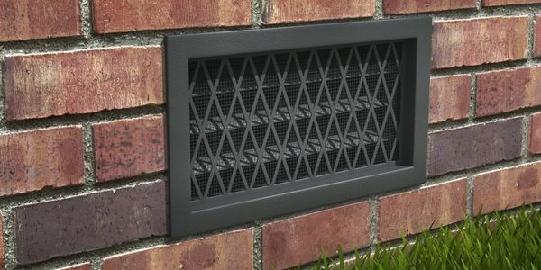Black metal vent grate on a red brick wall with grass below.