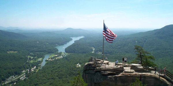 American flag on rocky overlook with scenic river and forest view.