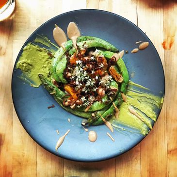 Artistic dish with green beans, sauce, and edible flowers on a blue plate.