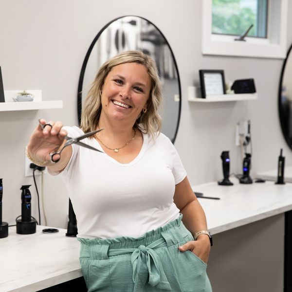 Smiling hairstylist holding scissors in a modern salon.