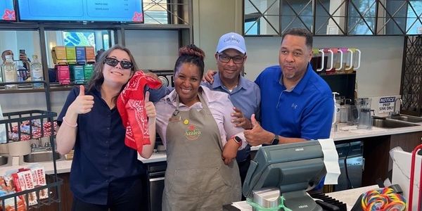 Group of four people smiling behind a counter in a cafe.