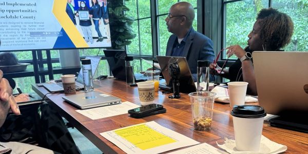 Colleagues engaged in a meeting around a wooden table with laptops and drinks.