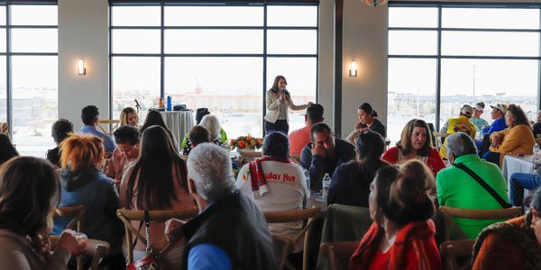 A woman speaks to an audience in a bright room.