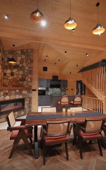 Cozy wooden cabin interior with dining area, stone fireplace, and modern kitchen.