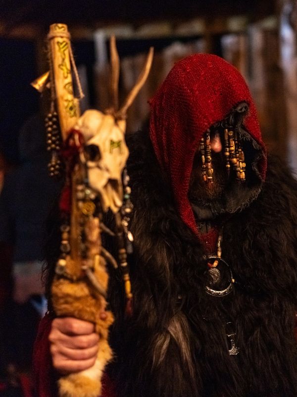 Person in red hood and fur holding a decorated staff.