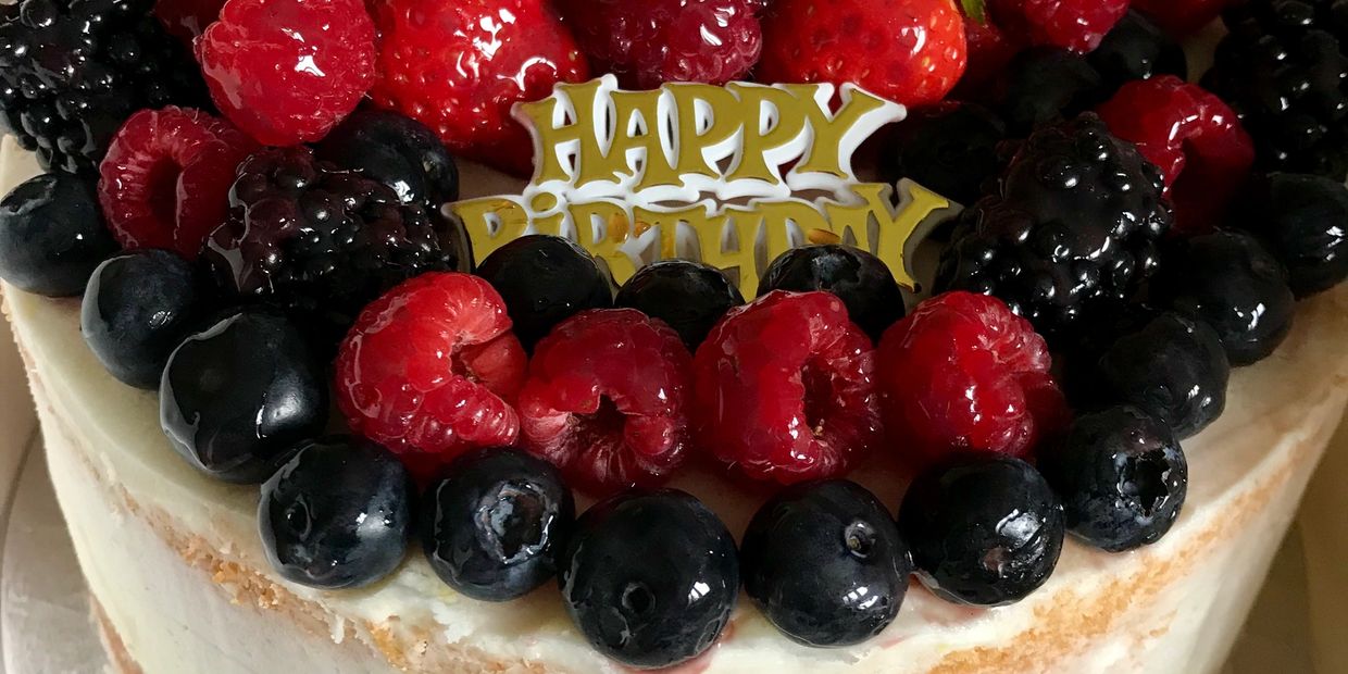 Semi naked celebration birthday cake with glazed fresh fruit topping.