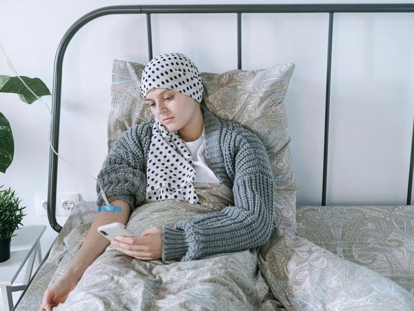 Woman in hospital bed with IV drip, looking at her phone.