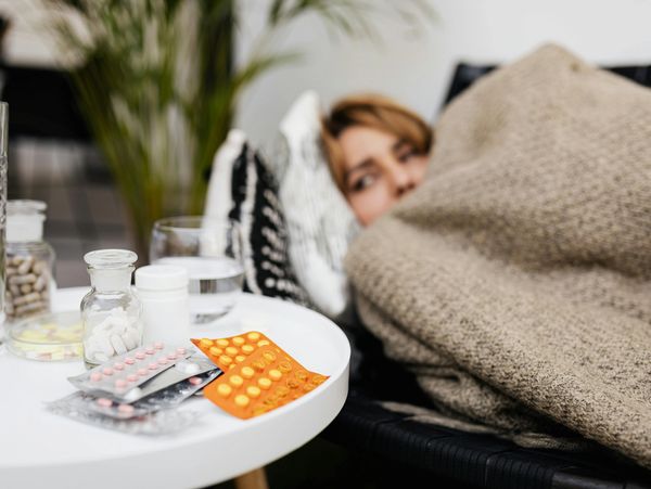 Person wrapped in blanket with medications and water nearby.