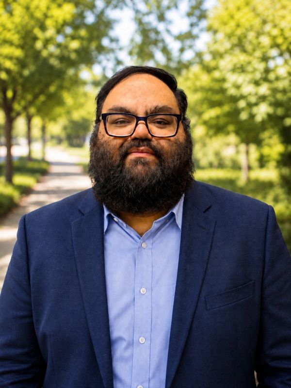 Man with glasses and beard wearing a blue blazer outside.