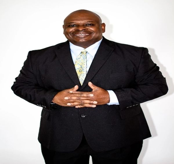Smiling man in a black suit with a patterned tie.