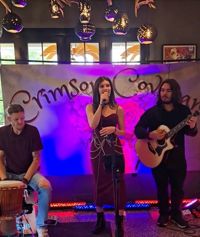 A trio performs live music with guitar, drums, and singing under decorative lights.