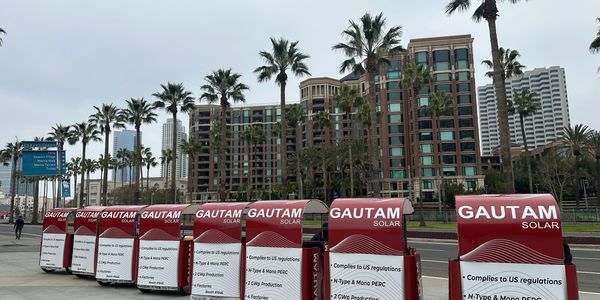 Row of Gautam Solar advertisement boards on a city sidewalk with palm trees.