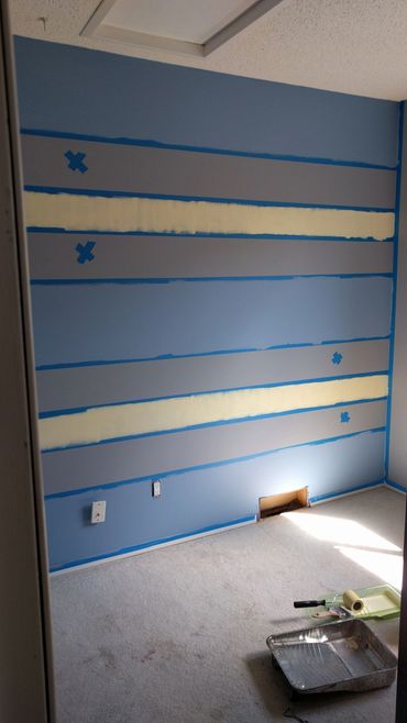 Room with striped wall painting in progress and painting supplies on carpet.