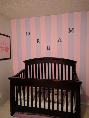 Dark wooden crib against pink and purple striped wall with 'DREAM' letters.
