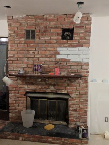A brick fireplace undergoing renovation with paint cans and tools.