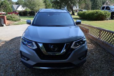 Front view of a silver Nissan SUV parked on a gravel driveway.