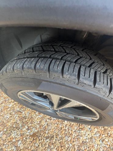 Close-up of a car tire and rim on gravel.