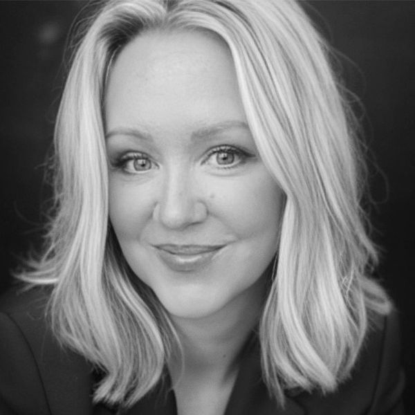 Smiling woman with blonde hair and blue eyes in a dark blazer.