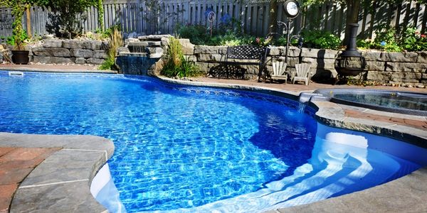Clear blue backyard swimming pool with stone edges and a waterfall.