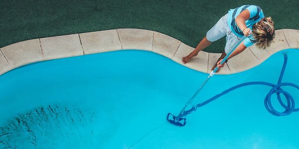 Person cleaning a swimming pool with a vacuum hose.