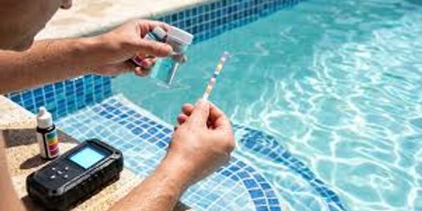Person testing pool water quality with testing strips and digital meter.