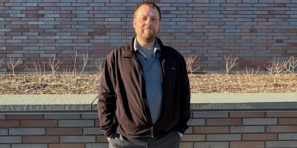 Man in black jacket standing against a brick wall.