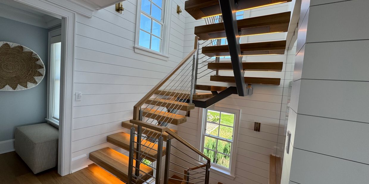 Modern wooden staircase with metal railing and warm lighting in a bright, white-paneled interior.