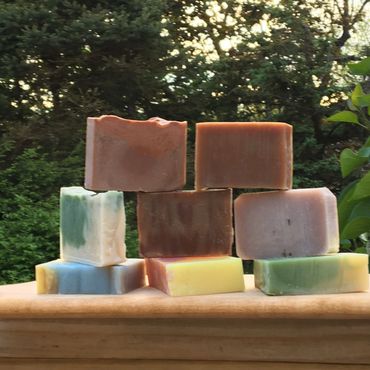 Stack of colorful handmade soap bars outdoors on a wooden surface.