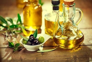 Bottles of olive oil and a bowl of green and black olives on a wooden table.