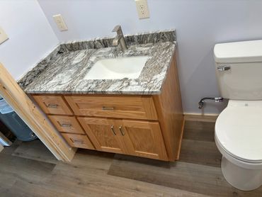 Bathroom vanity with granite countertop and white sink beside a toilet.