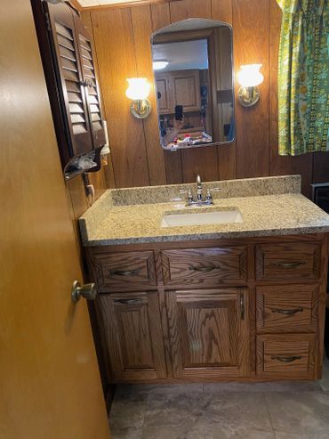 Vintage bathroom vanity with wood paneling and floral curtains.