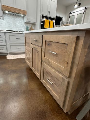 Close-up of a kitchen island with wooden cabinetry and a polished concrete floor.