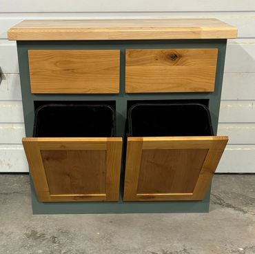 Wooden recycling bin with two tilt-out openings and two drawers above.