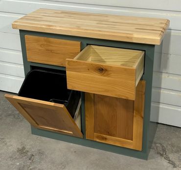 Wooden cabinet with open drawer and tilt-out trash bin.