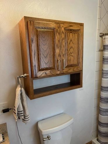 Wooden bathroom cabinet mounted above a toilet with a towel hanging beside it.