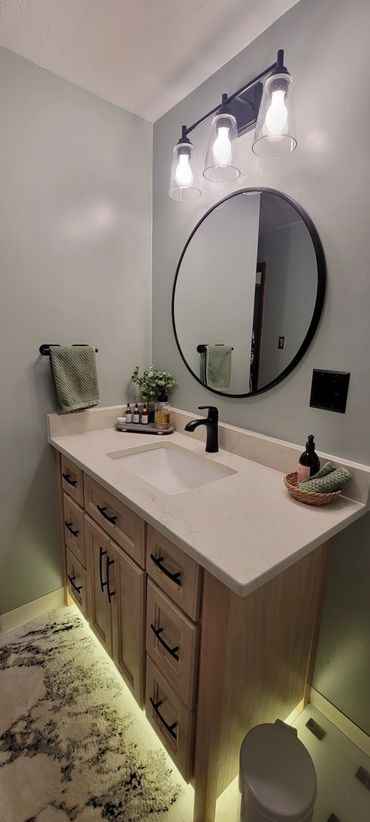 Modern bathroom vanity with round mirror and under-cabinet lighting.